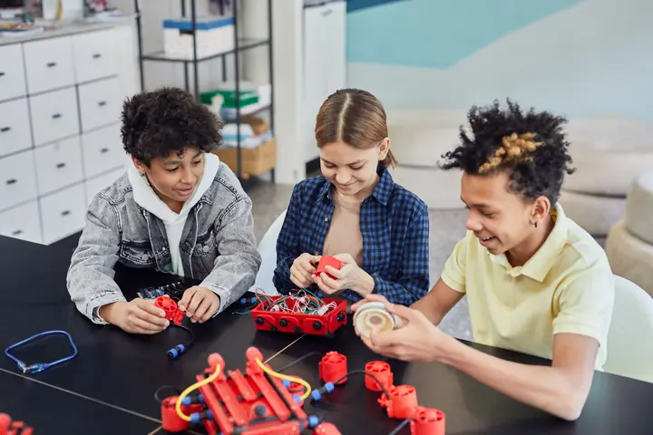 Young children sitting together on the floor, laughing while they build a small robot