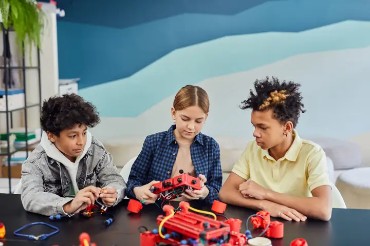 Children concentrating on an electronics kit, connecting components on a workbench