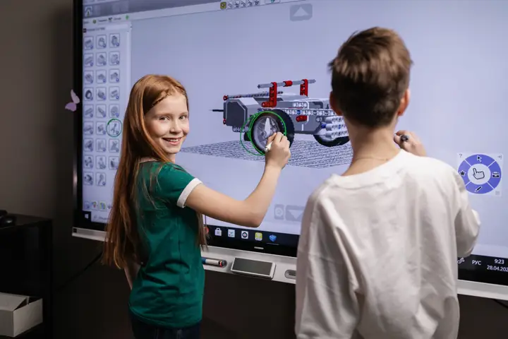 Two children standing at an interactive whiteboard, solving a puzzle together