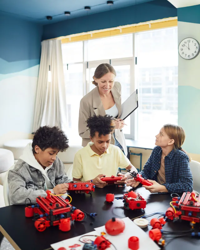 A teacher leaning in to help three children working on their robotics kits